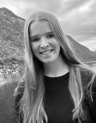 Headshot photo of Devin smiling with a scenic background.