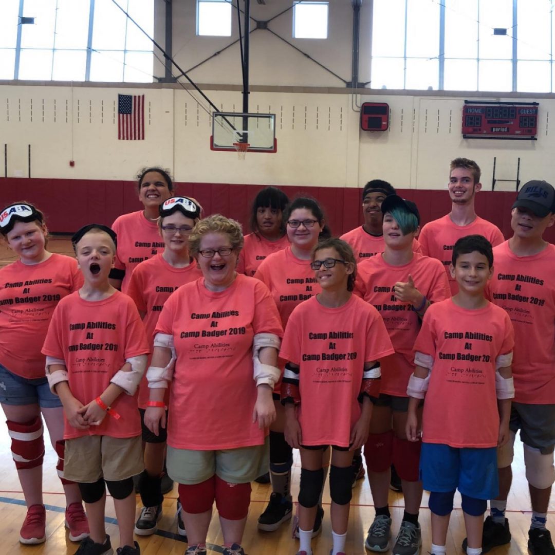 Whole group photo of athletes wearing pink Camp Badger tshirts. Some athletes are wearing elbow and kneepads and goalball blindfolds.