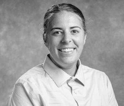 Alex smiling for photo wearing a collared shirt. Photo in greyscale.