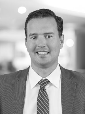 A headshot photo of Corey smiling wearing a suit and tie.