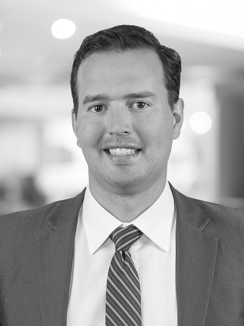 A headshot photo of Corey smiling wearing a suit and tie.