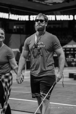 A photo of Evan walking holding hands with a lady. Evan is wearing sunglasses, a short sleeve shirt, and shorts.