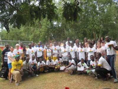 Group photo of Camp Abilities Ghana athletes and coaches. Most are wearing their white Camp Abilities Ghana tshirts with Ghana flag colors, red, green, yellow. Everyone is smiling. 