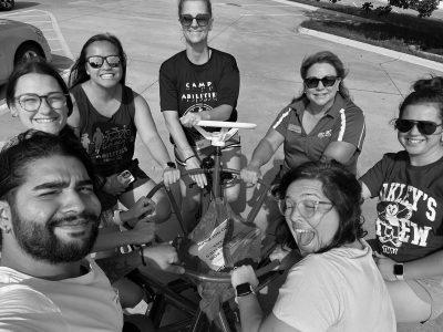 Group photo of athletes and coaches riding the 7-person bike at Camp Abilities Texas in greyscale.