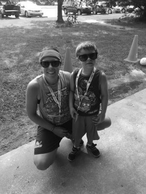 Alex squatting down and posing next to a standing male athlete. Alex and the athlete are both wearing sunglasses, medals around their necks, and a Teenage Mutant Ninja Turtle shirt.