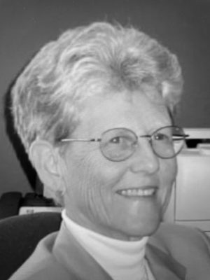 Headshot of Judy Byrd smiling and wearing glasses, white turtleneck shirt, and suit coat. Photo in greyscale.