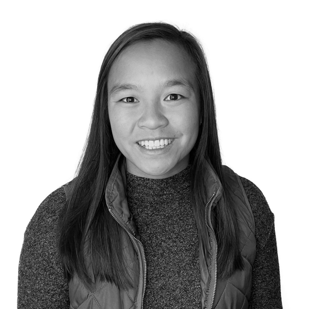 Lily smiling for photo wearing a sweater and vest. Photo is in greyscale.