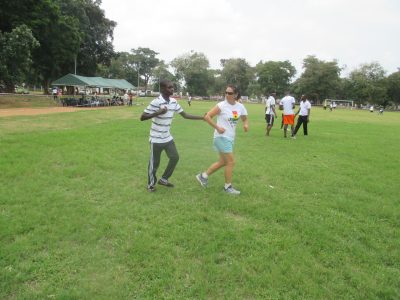 Lauren guiding athlete while running. Athlete is holding onto Lauren's bent arm. Running on grass with trees in background. Other athletes and coaches in background. 