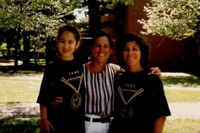 Dr. Lieberman with her arms around Monica and Maria Lepore. All three are smiling at the camera with a brick building and trees in the background. 