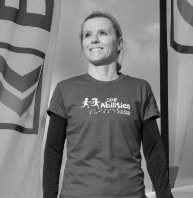 Photo of Valerie Caron standing and looking off to the distance in greyscale. Val is wearing a long sleeve shirt with a Camp Abilities Suisse shirt and leggings.
