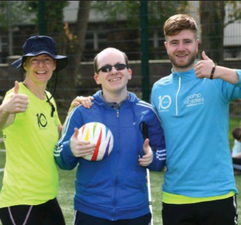 3 individuals smiling at the camera with their thumbs up in the air. The person in the middle is holding a soccer ball. 